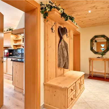 Ein heller Eingangsbereich mit Holzverkleidung und einem bequemen Schuhschrank. Im Hintergrund ist eine moderne Küche sichtbar, die gut ausgestattet ist.