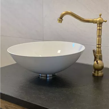 Ein modernes Waschbecken aus weißem Keramik mit einem goldenen Wasserhahn. Die Einrichtung ist schlicht und elegant.