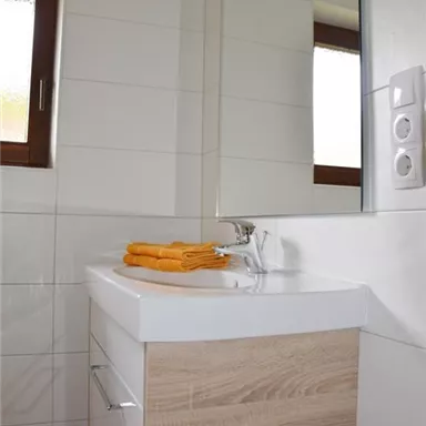 A modern bathroom with a minimally designed sink unit. There are bright tiles and large windows that provide plenty of light.