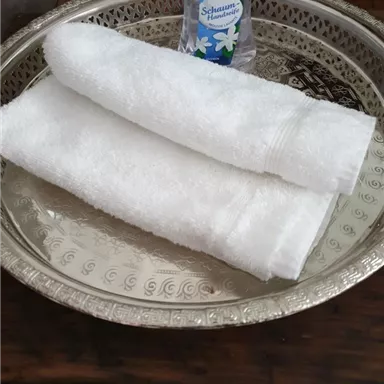 A silver tray with two white towels and a bottle of Palmolive hand soap. The presentation is simple and stylish.