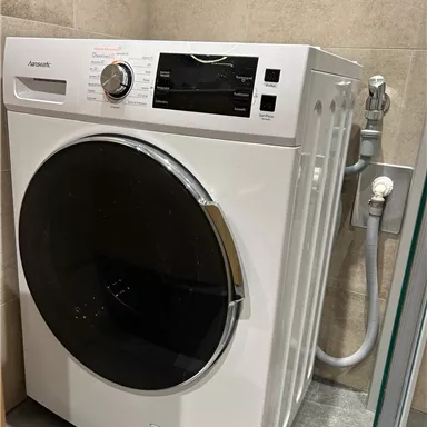 A modern washing machine in an elegant bathroom. It is standing against a wall and has a large porthole as well as various controls.