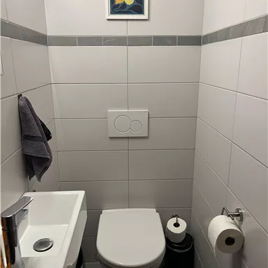 A modern small bathroom with white tiles. It includes a toilet, a sink, and decorative wall design.
