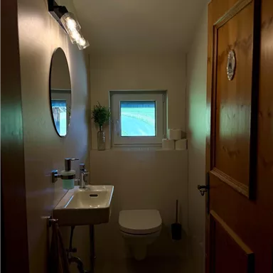 A modern bathroom with a sink, a toilet, and a small window. The room is bright and has a cozy atmosphere.