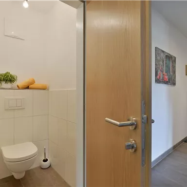 A modern guest bathroom with bright tiles and minimalist design. Decorative pictures hang on the wall, and the environment is well-lit.