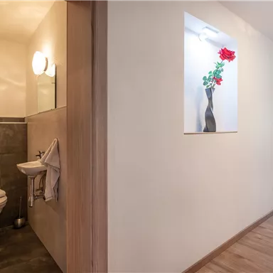 A bright hallway with a bathroom on the left side. On the wall, there is a vase decorated with a red rose.
