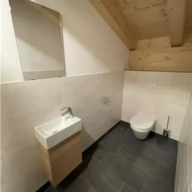 A modern bathroom with a wooden ceiling and tiled floor. It includes a sink and a toilet.