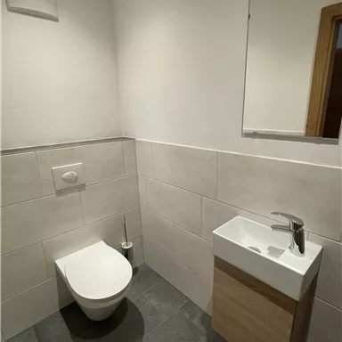 A modern bathroom with a toilet and a small sink. The walls are brightly tiled and the floor is dark.