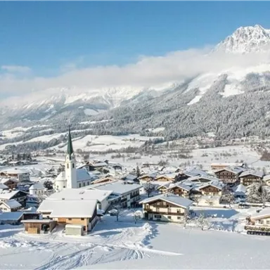A snowy mountain landscape with a small village in the foreground. The sky is clear and blue, and the surroundings are surrounded by snow-covered mountains.