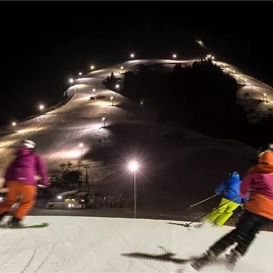 Nacht-Skifahren auf beleuchteten Pisten. Skifahrer in bunten Anzügen genießen die winterliche Atmosphäre.