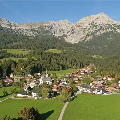 Eine malerische Berglandschaft mit einem kleinen Dorf in einem grünen Tal. Die Berge im Hintergrund sind majestätisch und klar.