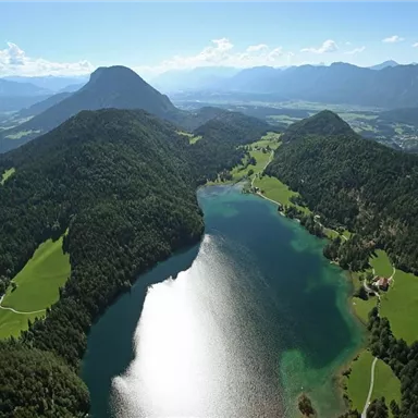 Eine beeindruckende Landschaft mit einem glitzernden See, umgeben von grünen Hügeln und Bergen. Der Himmel ist klar und strahlend blau.