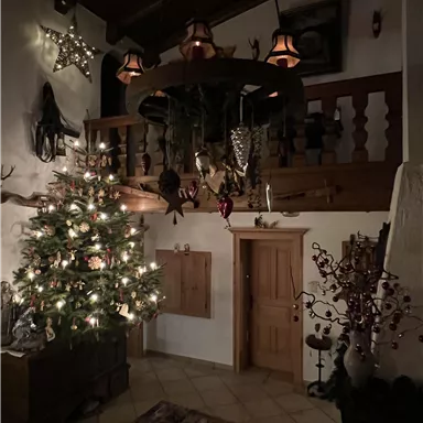 Ein gemütlicher Raum mit einem festlich geschmückten Weihnachtsbaum und warmem Licht. Die Wände sind mit Weihnachtsdekoration und Holzdetails versehen.