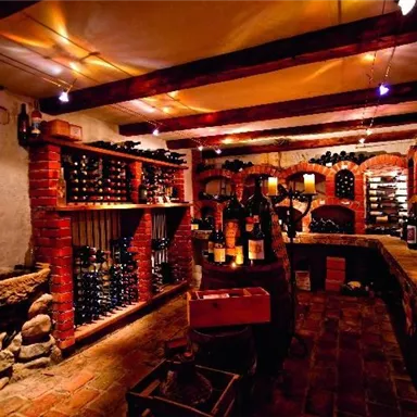 A cozy wine cellar with shelves full of wine bottles and warm light. The brick walls and rustic decor create an inviting atmosphere.