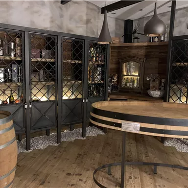 A cozy wine cellar with dark shelves and a round wooden table. In the background, wine barrels and decorative elements can be seen.
