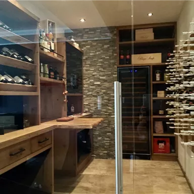 Ein eleganter Weinkeller mit Holzregalen und einer Glaswand. Die Wände sind mit Steinverkleidungen gestaltet und es gibt einen kleinen Tisch zum Verweilen.