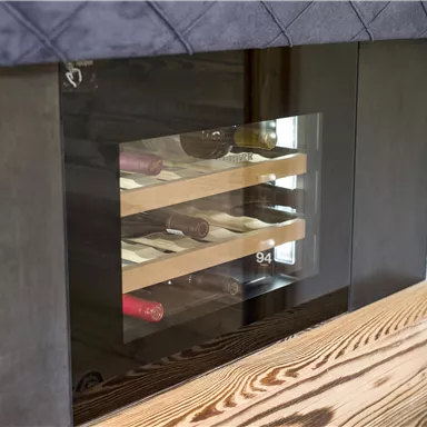 A modern wine rack with a glass cutout. It displays various wines on wooden shelves.