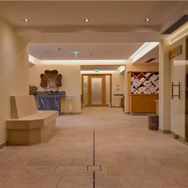 Ein heller und einladender Wellnessbereich mit modernen Elementen. Auf der linken Seite befinden sich Sitzgelegenheiten und eine Sauna in der Ecke.