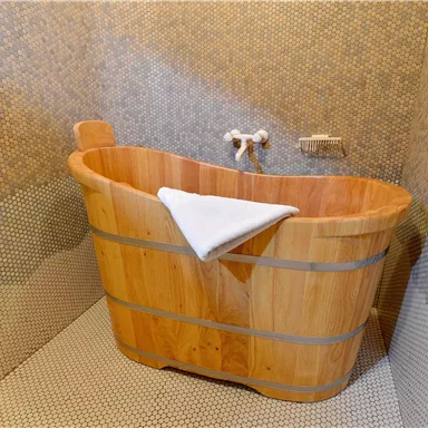 A cozy wooden bathtub is in a modern bathroom. The walls are decorated with small mosaic tiles.