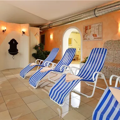 A relaxing wellness area with loungers in a blue and white striped pattern.  
Plants and soft lighting create a pleasant atmosphere.