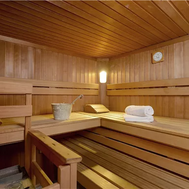 A cozy wooden sauna with benches and towels. A bucket and a clock are also in the room.
