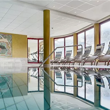 An elegant indoor pool with relaxing loungers in a bright room. Large windows offer a view of the greenery.
