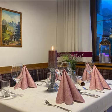 An elegantly set table with pink napkins and candles. In the background is a painting and a window with a view of the mountains.