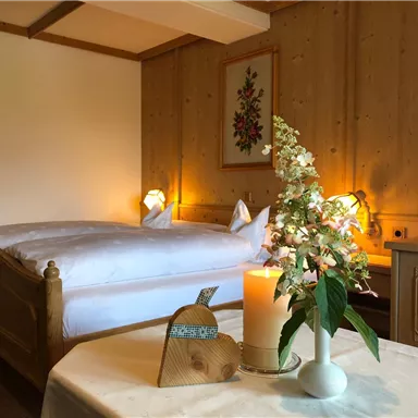 A cozy bedroom with wooden decor and two beds. On the table, there is a blooming plant and a candle that create a relaxed atmosphere.