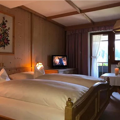 A cozy room with two beds and wooden paneling. A candle is on the table, and a television is visible in the background.