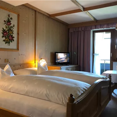 A cozy bedroom with two beds and traditional wooden furniture. A window with a view outside and a television are also available.