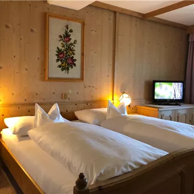 A cozy bedroom with two single beds, wooden paneling, and soft lighting. A television is also available, and a wall decoration with floral design complements the room.