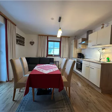 A cozy kitchen with a dining area and wooden floor. Large windows provide plenty of daylight.