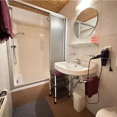 A small bathroom with a shower, sink, and mirror. It is modern and well-equipped.