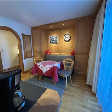 A cozy room with a table and two chairs. The walls are made of wood, and there is a decorative clock as well as some plants.