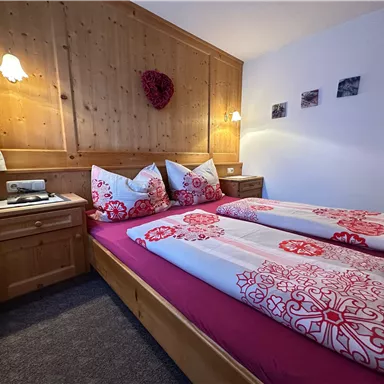 A cozy bedroom with two single beds and decorative pillows. The walls are made of wood and there is warm lighting for an inviting atmosphere.