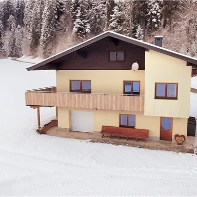 Ein gemütliches Haus in einer verschneiten Landschaft. Umgeben von Bäumen und frischem Schnee, schafft es eine einladende Atmosphäre.