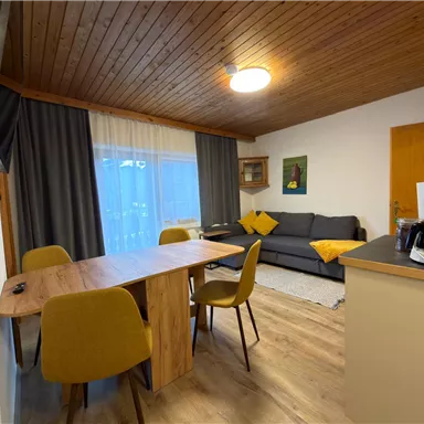 A cozy living room with a dining area and a sofa. Large windows provide plenty of daylight.