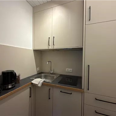 Eine moderne Küche mit hellen Schränken und einer kleinen Spüle. Die Ausstattung umfasst eine Kaffeemaschine und einen handtuch um die Spüle.