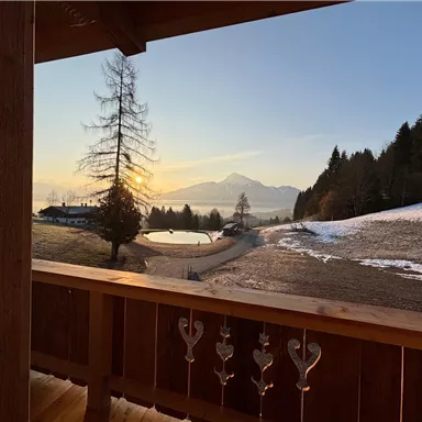 A beautiful view from the balcony with a sunset over the mountains. The landscape is surrounded by snow and trees.