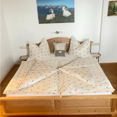 Ein gemütliches Doppelbett mit dekorativen Kissen und einer hellen Bettwäsche. Im Hintergrund hängen Bilder von der Landschaft an der Wand.