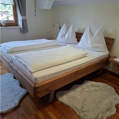 A cozy bedroom with a large double bed and two pillows. Soft carpets and natural wood surfaces create a warm atmosphere.