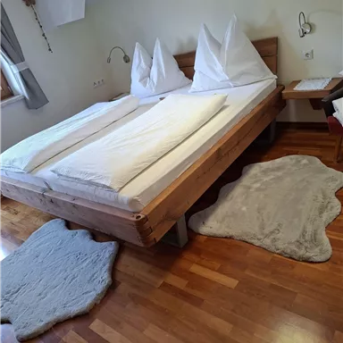 A cozy bedroom with a large double bed and two pillows. The floor is made of wood with soft carpets.