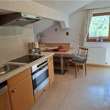 A modern kitchen with wooden cabinets and a comfortable dining area. Large windows provide plenty of natural light and a view outside.