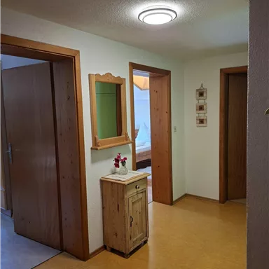 A bright hallway with two doors and a small wooden piece of furniture. On the wall hangs a mirror and a decoration.