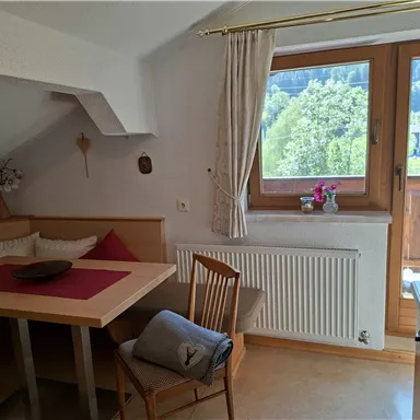 A cozy dining area with a wooden table and chairs. Through the window, a beautiful view of nature is visible.