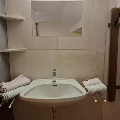A modern bathroom with a simple sink and a large mirror. Two pink towels are lying on the shelf.