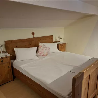 A cozy bedroom with a wooden double bed and two nightstands. The walls are light and the room feels inviting.