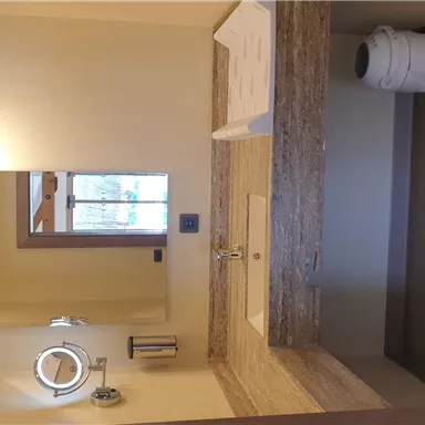 Ein modernes Badezimmer mit einer eleganten Waschbeckenablage. Im Hintergrund ist ein Spiegel und ein Fenster sichtbar.