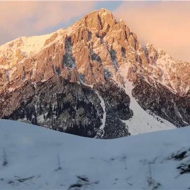 Ein majestätischer Berg mit schneebedecktem Gipfel und sanften Hängen. Der Himmel zeigt sanfte Farbtöne bei Sonnenuntergang.