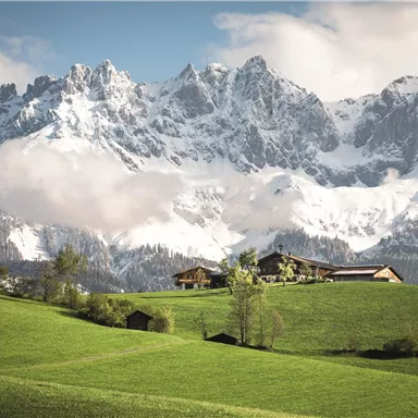 A beautiful mountain panorama with snow-covered peaks and lovely clouds. In the foreground, lush green meadows and a picturesque landscape stretch out.