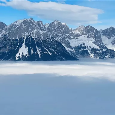 An impressive mountain landscape with snow-covered peaks. Below lies a sea of fog that makes the view even more dramatic.